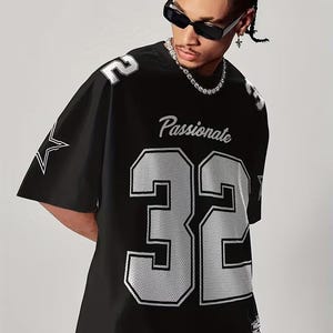 A man wearing a black mesh football jersey with the number 32, sunglasses, and a necklace.