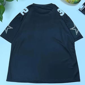 A black mesh football jersey with white stars on the sleeves is displayed on a light blue background.