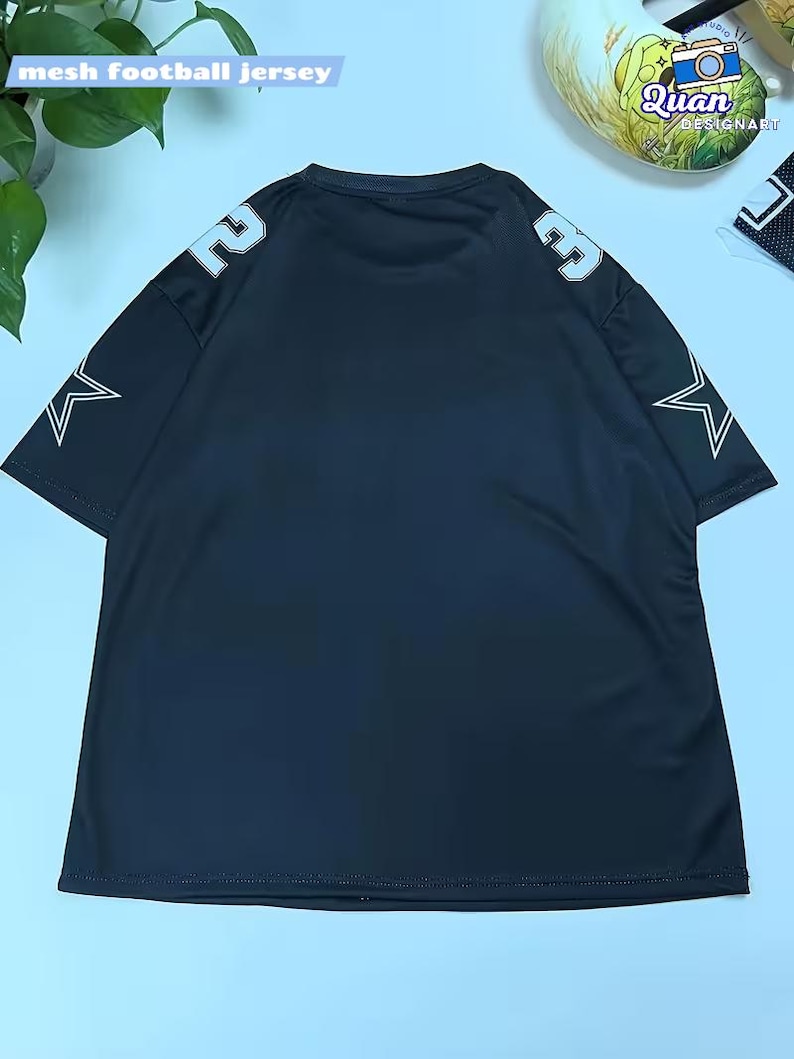 A black mesh football jersey with white stars on the sleeves is displayed on a light blue background.