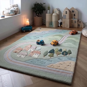 May include: A rectangular children's play rug with a town and road design. The rug features a light green background with a road, houses, trees, and a river. Three toy cars are on the rug. The rug is on a hardwood floor.
