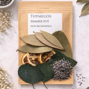 May include: A brown paper packet labelled "THIMELESS SIMMER POT NEW BEGINNINGS" with dried bay leaves, eucalyptus leaves, dried lemon slices, and lavender buds. A small white bowl of lavender buds is in the upper left corner.