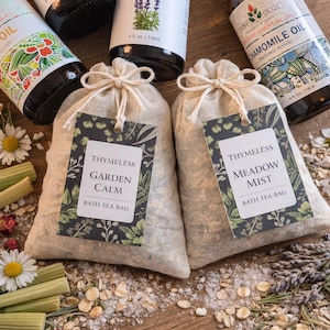 May include: An arrangement of essential oil bottles and bath tea bags. The bottles are labelled with names such as "Lemongrass" and "Chamomile Oil." Two linen bags with tags reading "Thymeless Garden Calm" and "Thymeless Meadow Mist" are in the foreground.
