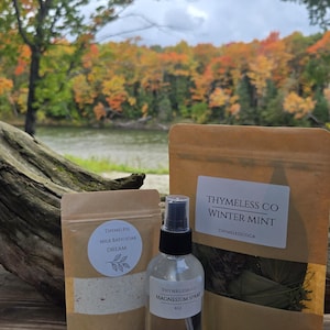 May include: A clear spray bottle labelled Thymeless Co Magnesium Spray 4oz, a small brown pouch labelled Thymeless Milk Bath Soak Dream, and a larger brown pouch labelled Thymeless Co Winter Mint with the website address Thymelessco.ca printed below.