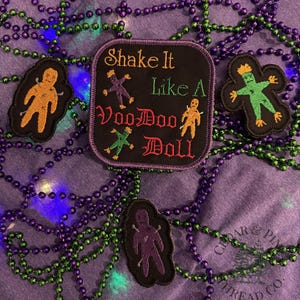 May include: A collection of embroidered patches and beads. The patches feature voodoo doll designs and the text "Shake It Like A VooDoo Doll". The beads are purple and green.