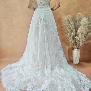 Puede incluir: Vestido de novia blanco sin tirantes de encaje con una larga cola. La parte trasera del vestido presenta un cierre tipo cors&eacute; con un lazo. El vestido est&aacute; hecho de encaje delicado y es largo.