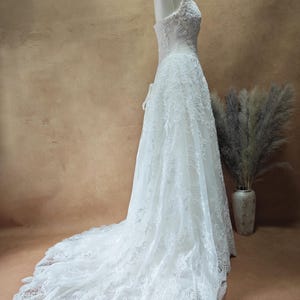 Puede incluir: Un vestido de novia blanco sin tirantes con intrincados detalles de encaje. El vestido presenta un corpi&ntilde;o ajustado y una falda fluida que se extiende en una larga cola. El vestido se exhibe en un maniqu&iacute;.