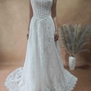 Puede incluir: Vestido de novia blanco sin tirantes con encaje. El vestido tiene una falda fluida y una cola. El corpi&ntilde;o est&aacute; adornado con intrincados patrones de encaje floral. Vestido largo, ideal para una boda o evento formal.