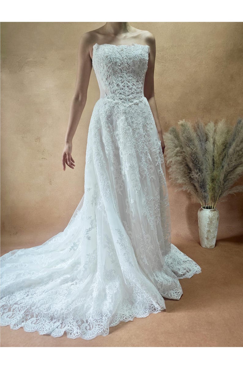 Vestido de novia de encaje con cintura vasca y sin tirantes imagen 1