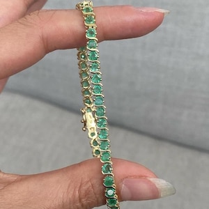 May include: A gold bracelet featuring a series of oval-cut emeralds. The emeralds are set in a gold band, creating a continuous line of green gemstones. The bracelet is secured with a clasp.