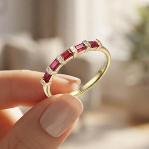 Puede incluir: Un anillo de oro con una hilera de cinco rubíes rojos de corte baguette rectangular que se alternan con pequeños diamantes blancos redondos, engastados en un estilo de canal a lo largo de la mitad superior de la banda.