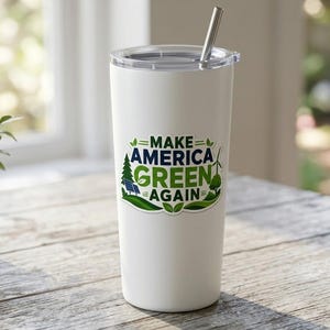 May include: A white stainless steel tumbler with a clear lid and a metal straw. The front features a graphic with the text "MAKE AMERICA GREEN AGAIN" in blue and green, surrounded by illustrations of a pine tree, solar panels, and a wind turbine.