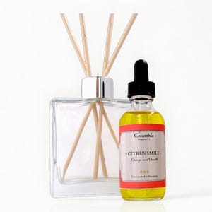 May include: A clear glass diffuser with wooden reeds and a bottle of Citrus Smile fragrance. The fragrance bottle has a black dropper and a red and white label that reads "Orange and Vanilla".