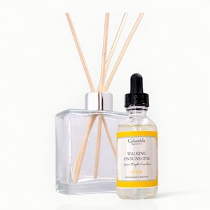 May include: A clear glass diffuser bottle with wooden reeds and a small glass bottle with a black dropper. The small bottle has a yellow label with the text "WALKING ON SUNSHINE" and "Columbia Fragrance Co."