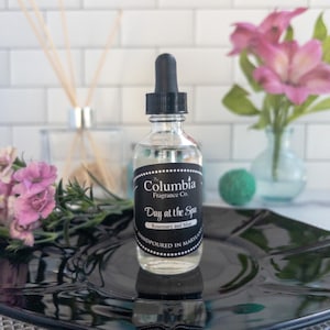 May include: A clear glass bottle with a black dropper top and a black label that reads "The Columbia Fragrance Co. Day at the Spa Rosemary and Mint Handpoured in Maryland"