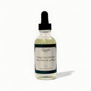 Könnte beinhalten: Eine klare Glasflasche mit schwarzem Tropfverschluss. Auf dem Etikett steht "THYME TO UNWIND" mit "Hilton White Tea and Thyme" und "Columbia Fragrance Co." Die Flasche enthält eine hellgelbe Flüssigkeit und wird in Maryland von Hand abgefüllt.