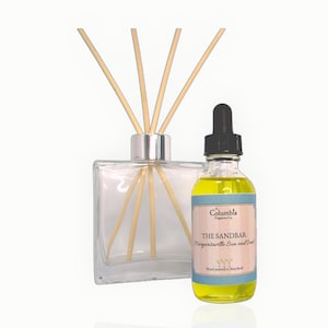 May include: A clear glass diffuser with wooden reeds and a bottle of oil. The oil bottle has a black dropper and a label that reads "THE SANDBAR Margaritaville Sun and Sea" with the Columbia Fragrance Co. logo.