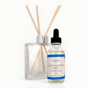 May include: A clear glass diffuser bottle with wooden reeds and a small glass bottle with a black dropper. The small bottle has a blue and white label that reads "MEDITERRANEAN MAGIC - Smell the Happy!" and "Columbia Fragrance Co."