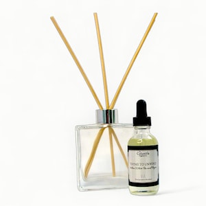 May include: A clear glass diffuser with wooden reeds and a small glass bottle with a black dropper. The bottle has a black and white label that reads "Thyme to Unwind" and "White Tea and Thyme". The products are for home fragrance.
