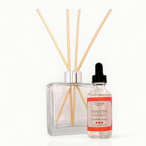 May include: A clear glass diffuser with wooden reeds and a small bottle of fragrance oil. The oil bottle has a red label with the text "PARADISE - FOUND - Smell the Happy!" and a black dropper.