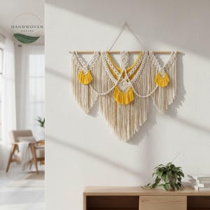 May include: A handcrafted macrame wall hanging with a natural, off-white color scheme and accents of yellow. The design features intricate knotting patterns, a wooden dowel, and a fringed bottom, adding a bohemian touch to home decor.