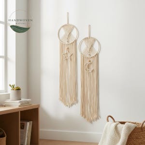 Op de afbeelding: Twee crèmekleurige macramé wandkleden. Eén heeft een ster, de andere een halve maan, opgehangen in cirkelvormige frames. Lange, gefranjerde strengen hangen eronder. Het logo "HANDWOVEN NATURE" staat linksboven.