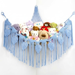 May include: A light blue macrame hammock-style storage unit filled with stuffed animals. The hammock is decorated with leaf-shaped accents and long fringe. The unit is mounted in a corner, providing a decorative and functional storage solution.