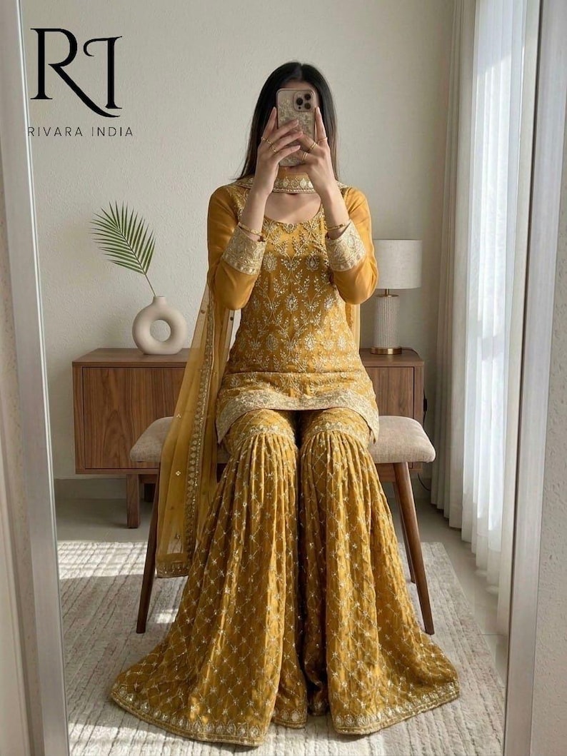 May include: Mustard yellow embroidered salwar kameez set. The set includes a long-sleeved top, wide-legged pants, and a matching scarf. The outfit features intricate gold embroidery and is from Rivara India.