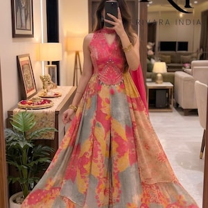 Puede incluir: Un vestido largo con cuello halter y un estampado floral brillante. El corpiño está adornado con bordados y borlas detallados. El texto "RIVARA INDIA" es visible.