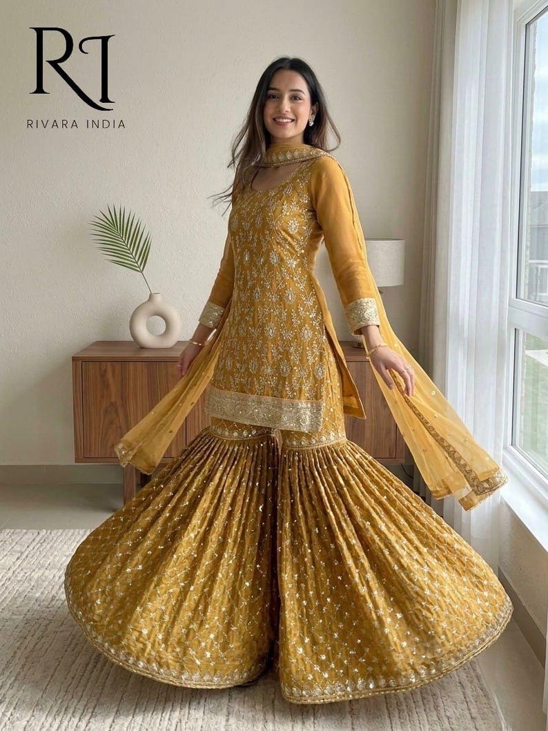 May include: Mustard yellow Indian salwar kameez set. The outfit features a long-sleeved tunic with intricate embroidery and flared pants. A matching scarf completes the ensemble. The outfit is embellished with silver accents and is suitable for festive occasions.
