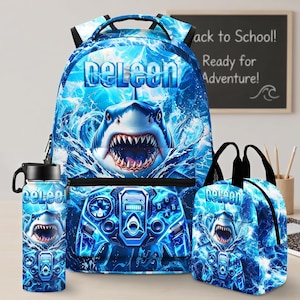 Könnte beinhalten: Ein blaues Set aus Rucksack, Lunchtasche und Trinkflasche mit einer Grafik eines aus dem Wasser auftauchenden Hais und einem Videospiel-Controller. Der Schriftzug "DELEON" ist auf jedem Teil in hellblauer Schrift vor Wasserhintergrund gedruckt.
