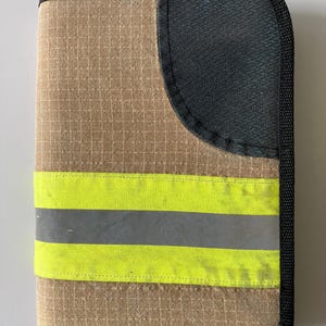 Könnte beinhalten: Beige-schwarzes Etui mit Reißverschluss und gut sichtbarem Design. Das Etui hat ein Gittermuster, eine schwarze Netztasche und zwei horizontale reflektierende Streifen in Neongelb und Grau. Oben ist eine schwarze Schlaufe angebracht.