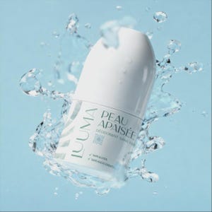 Peut inclure: Un déodorant blanc avec le texte "LUMA PEAU APAISÉE" et "DÉODORANT SANS PARFUM" est entouré de gouttelettes d'eau et d'éclaboussures sur un fond bleu clair. Le produit a un design minimaliste avec une esthétique épurée et moderne.