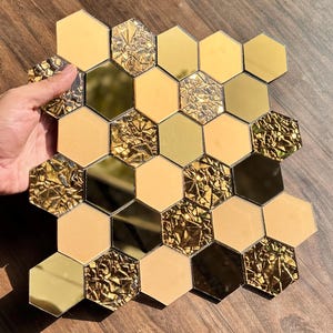 May include: Hexagonal tiles in shades of gold, beige, and mirrored surfaces. Some tiles have a textured, crumpled foil appearance. The tiles are arranged in a grid pattern, creating a decorative mosaic.