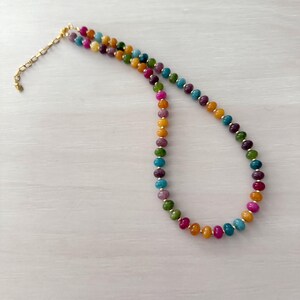 May include: A colorful beaded necklace with a gold-toned chain and clasp. The necklace features a variety of round beads in shades of pink, orange, yellow, green, blue, and purple. The beads are strung together to create a vibrant and eye-catching accessory.