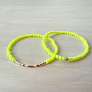 May include: Two neon yellow beaded bracelets with a gold bar clasp. One bracelet has a gold bead accent.