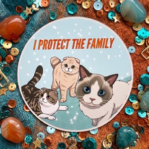 May include: A circular sticker with a light blue background featuring three illustrated cats and the orange text I PROTECT THE FAMILY. The cats include a brown tabby, a light tan cat, and a white and brown cat with blue eyes.