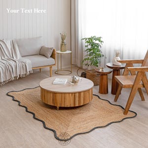 May include: A rectangular jute rug with a scalloped black border edge, featuring a natural tan woven texture. The rug is placed under a round wooden coffee table with a slatted base, a light grey sofa with a throw blanket, and a wooden chair.