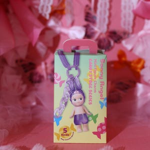 May include: A boxed Sonny Angel Candy Store Series mini figure charm. The box is light green with a pink handle and features a small doll with a purple outfit and bunny ears. The charm is attached to a purple chain.