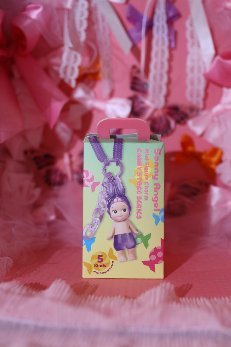 May include: A boxed Sonny Angel Candy Store Series mini figure charm. The box is light green with a pink handle and features a small doll with a purple outfit and bunny ears. The charm is attached to a purple chain.