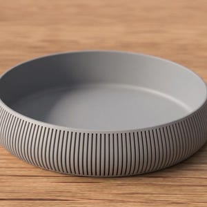 May include: A gray, round bowl with a ribbed exterior. The bowl has a smooth interior and sits on a wooden surface. The bowl's design features vertical lines around the sides.