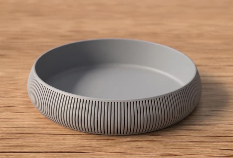 May include: A gray, round bowl with a ribbed exterior. The bowl has a smooth interior and sits on a wooden surface. The bowl's design features vertical lines around the sides.