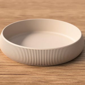 May include: A beige, round bowl with a ribbed exterior. The bowl sits on a wooden surface. The bowl's interior is smooth and the exterior has vertical lines. The bowl is a neutral color and could be used for serving or display.
