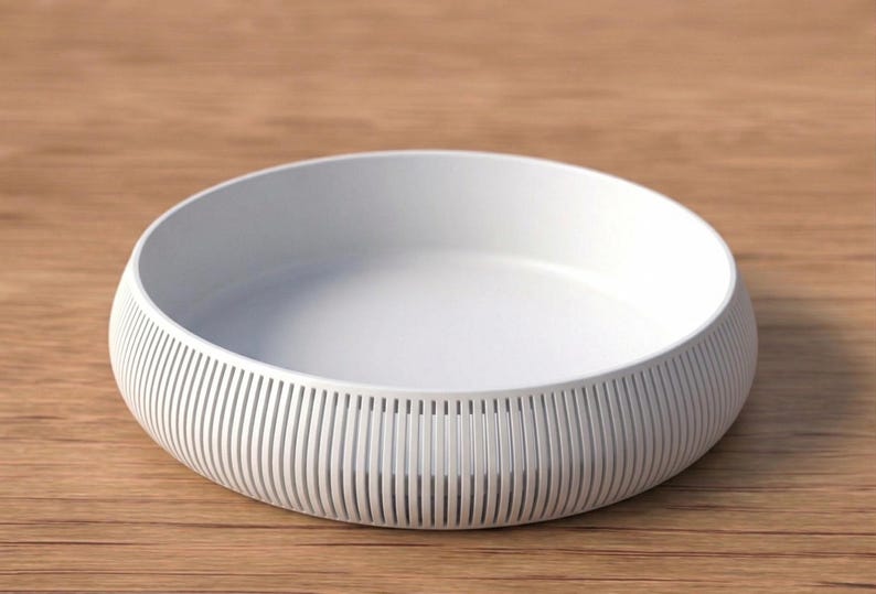 May include: A white, round bowl with a ribbed exterior design. The bowl has a shallow depth and sits on a wooden surface. The bowl's design features vertical lines around the exterior, creating a textured appearance. The bowl is likely used for serving or display.