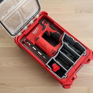 Peut inclure: Un ensemble d'outils électriques rouges et noirs dans un étui rouge avec un couvercle transparent. L'étui est ouvert, révélant l'outil et divers accessoires dans des compartiments gris. La marque "Milwaukee" est visible.