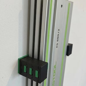 May include: A silver and green Festool FS 800/2 guide rail system mounted on a white wall. The rail has green accents and black mounting brackets. The text "FESTOOL" and "FS 800/2" are visible.