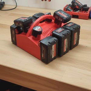 May include: A red Milwaukee battery charging station with multiple black battery packs. The station has a handle and is designed to hold and charge several batteries simultaneously. The batteries are labeled with the Milwaukee logo and product information.