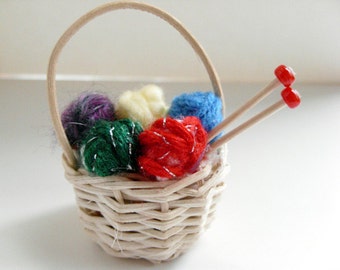 Puede incluir: Una cesta de mimbre blanca llena de ovillos de lana de colores y agujas de tejer. La lana es roja, verde, azul, morada y amarilla.