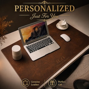 Puede incluir: Un tapete de escritorio de cuero marrón con el texto "ILO Dream it. Do it". Una computadora portátil, un ratón, un altavoz y una taza de té están sobre el tapete. Las palabras "PERSONALIZADO Just For You" están en la parte superior. El tapete está etiquetado como "Cuero genuino" y "Regalo perfecto".