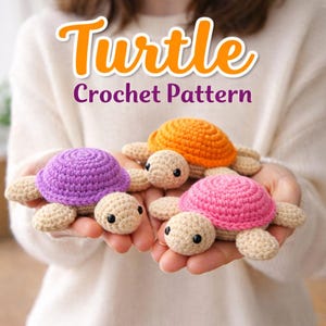 以下が含まれることがあります： 紫、オレンジ、ピンクの3匹のかぎ針編みのカメのおもちゃ。ベージュの頭と手足があります。「Turtle Crochet Pattern」の文字がカメの上にオレンジと紫で表示されています。