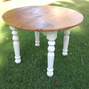 May include: A round wooden table with a natural wood top and white painted legs. The table has a simple, farmhouse style.